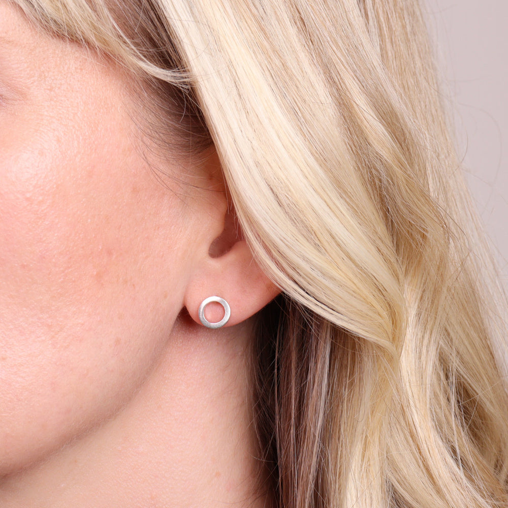 Brushed sterling silver circular stud earrings worn on ear