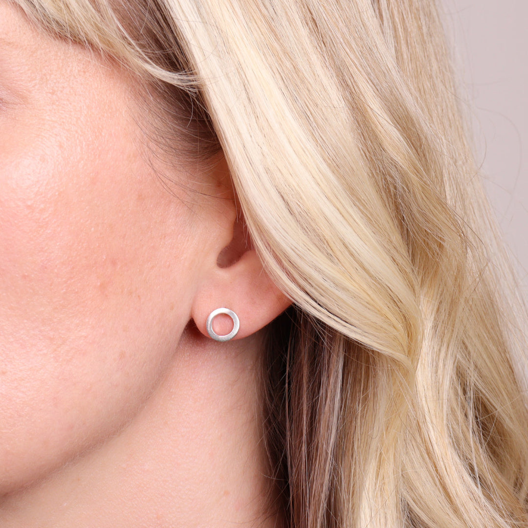 Brushed sterling silver circular stud earrings worn on ear