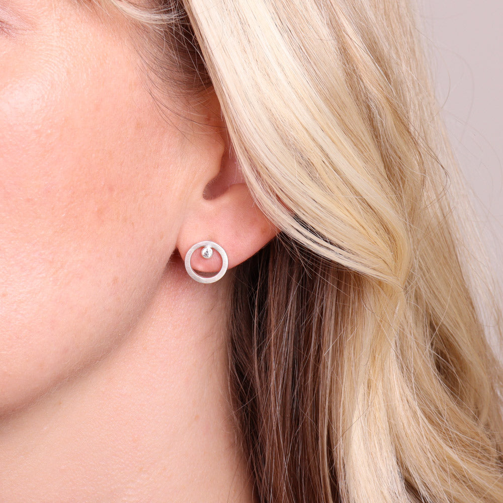 Frosted sterling silver circular stud earrings with moissanite worn on ear