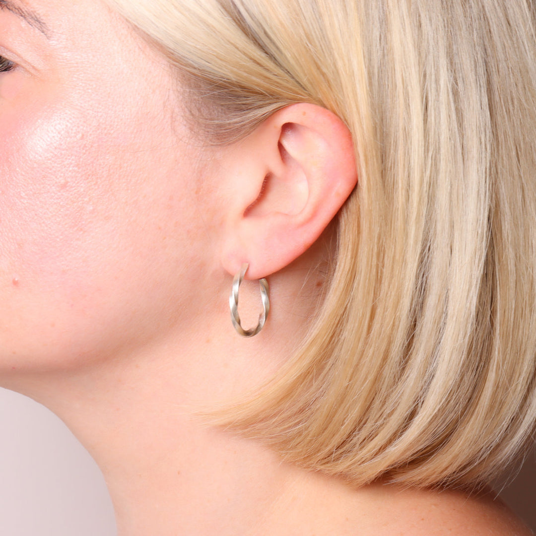 Brushed silver twisted hoop earrings worn on the ear