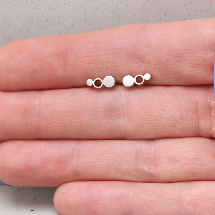 Geometric sterling silver stud earrings shown on hand for scale