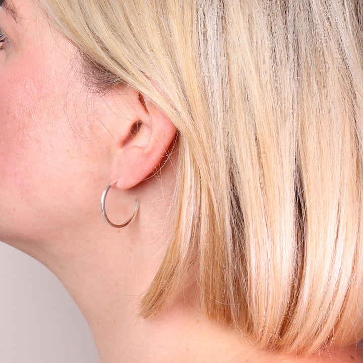 Large brushed sterling silver hoop earrings worn on the ear