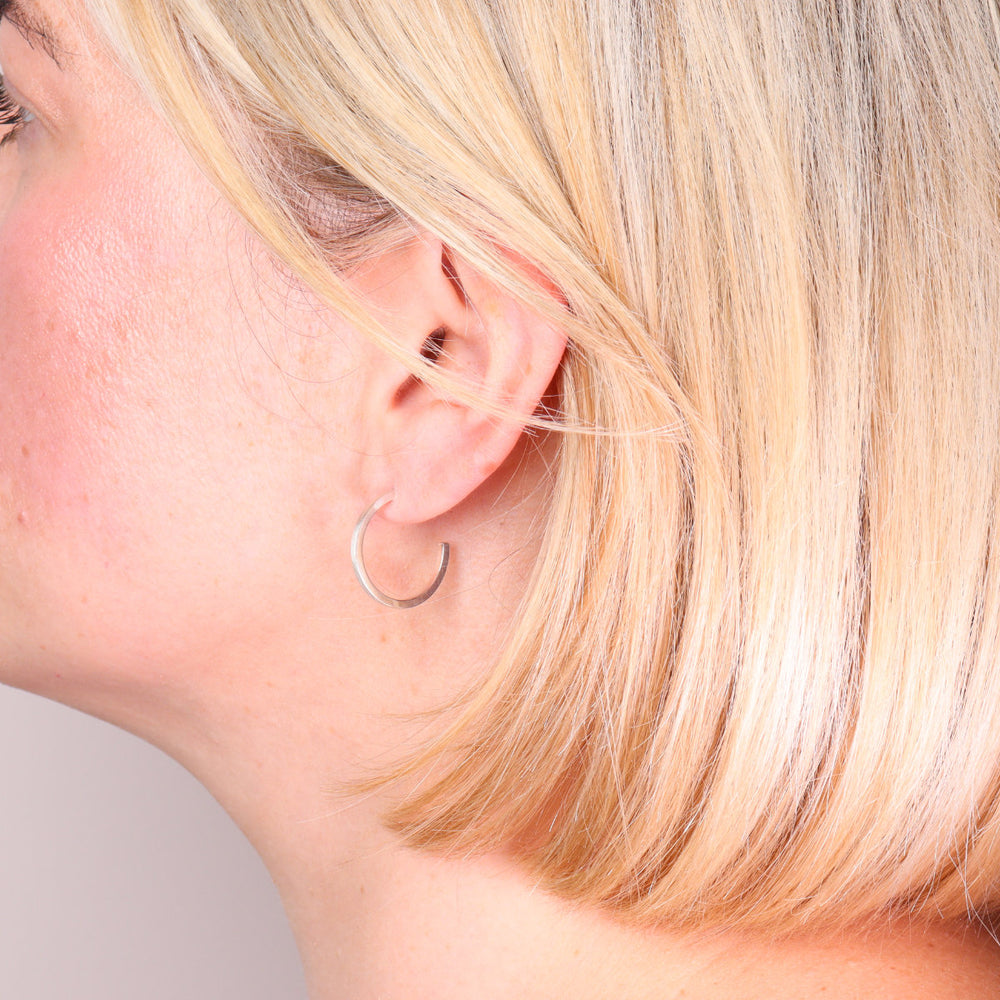 Medium brushed sterling silver hoop earrings worn on the ear