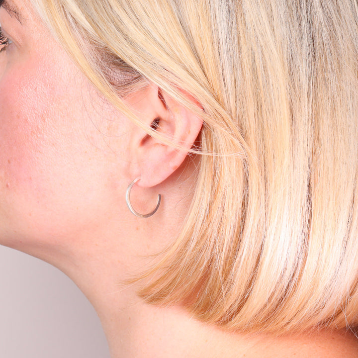 Medium brushed sterling silver hoop earrings worn on the ear