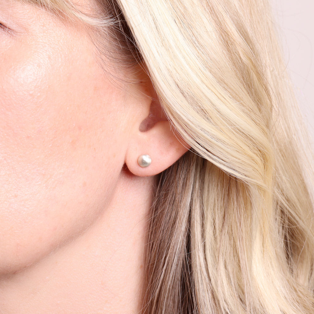Medium frosted silver stud earrings worn on the ear
