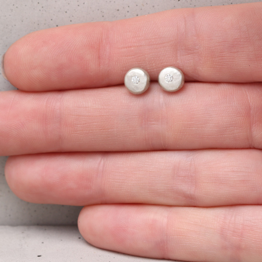 Recycled silver moissanite pebble stud earrings shown on hand for scale