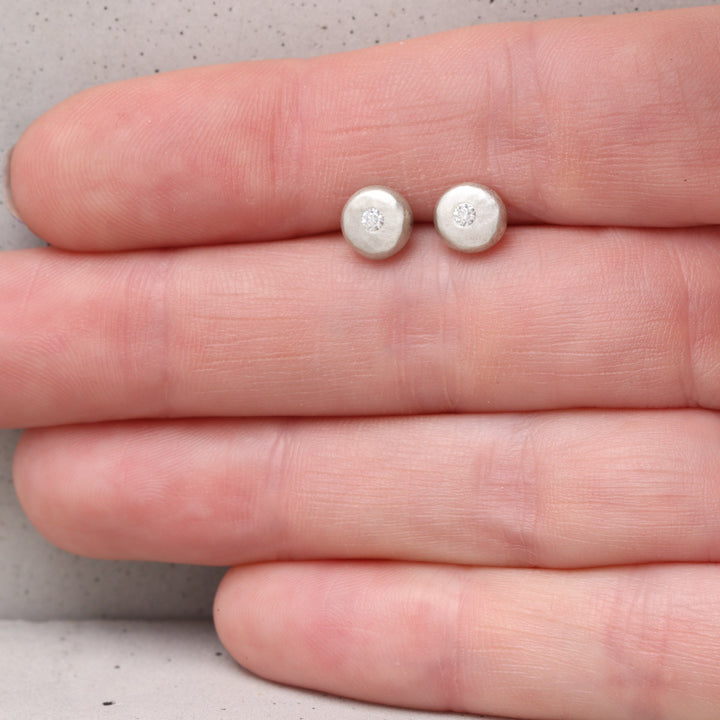 Recycled silver moissanite pebble stud earrings shown on hand for scale