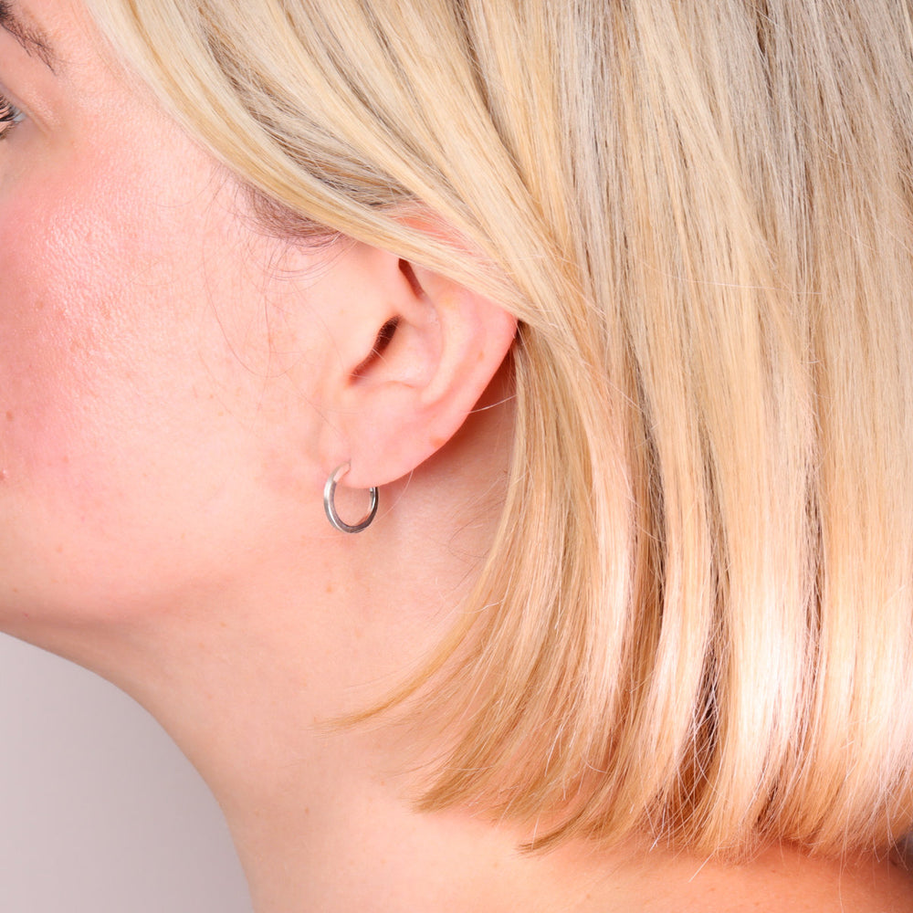 Small brushed sterling silver hoop earrings worn on the ear
