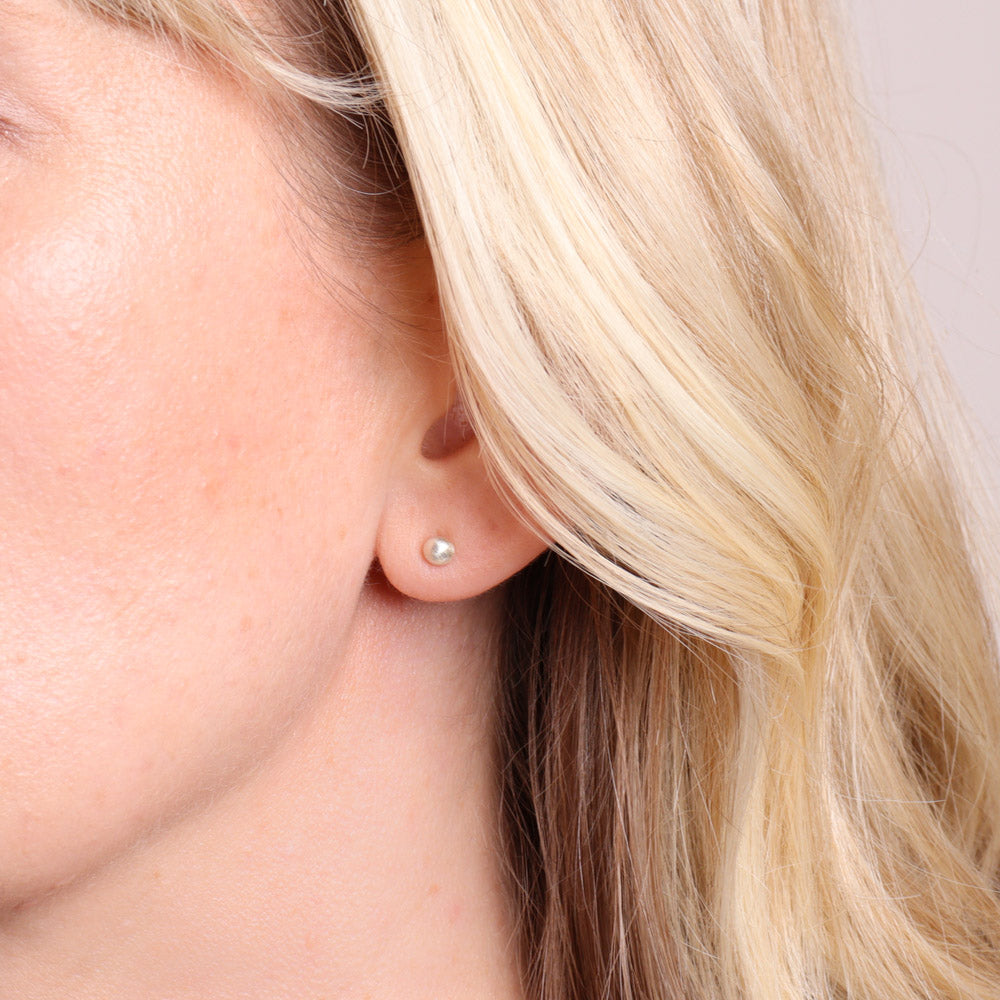 Small frosted silver stud earrings worn on the ear