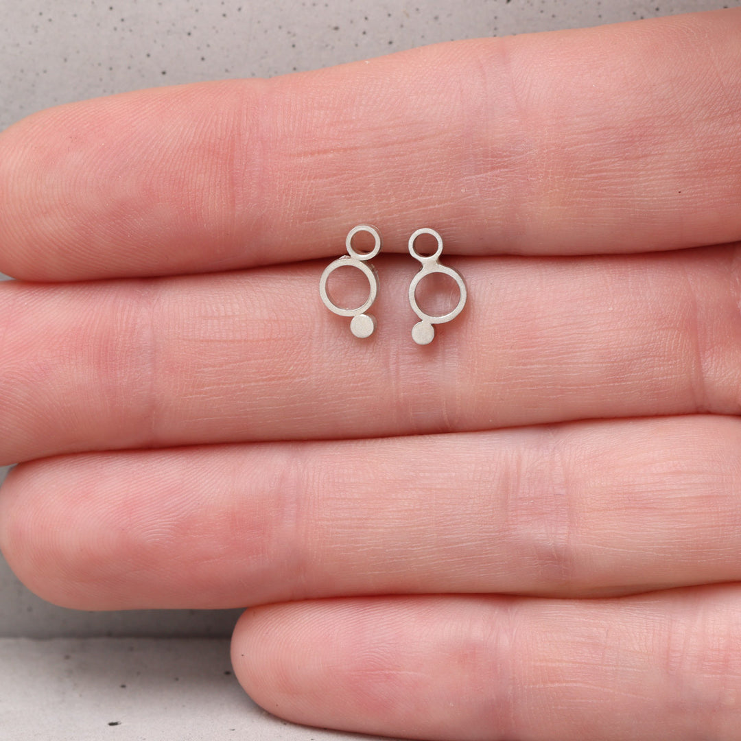 Sterling silver geometric circle stud earrings shown on hand for scale