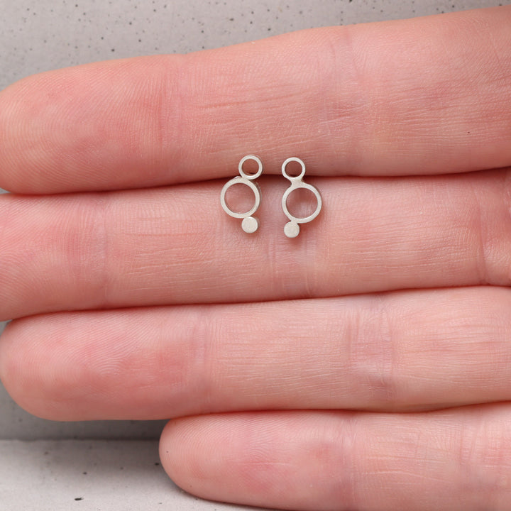 Sterling silver geometric circle stud earrings shown on hand for scale