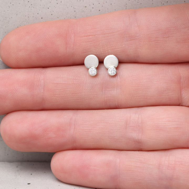 Sterling silver and moissanite stud earrings shown on hand for scale