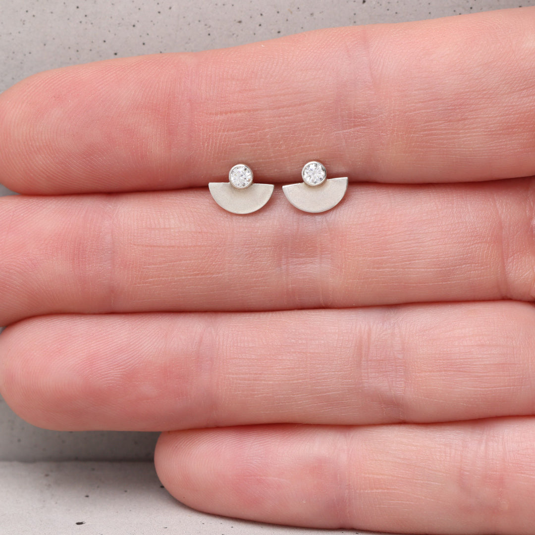 Sterling silver and moissanite stud earrings shown on hand for scale