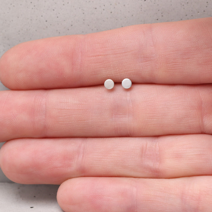 3mm sterling silver circle stud earrings shown on hand for scale