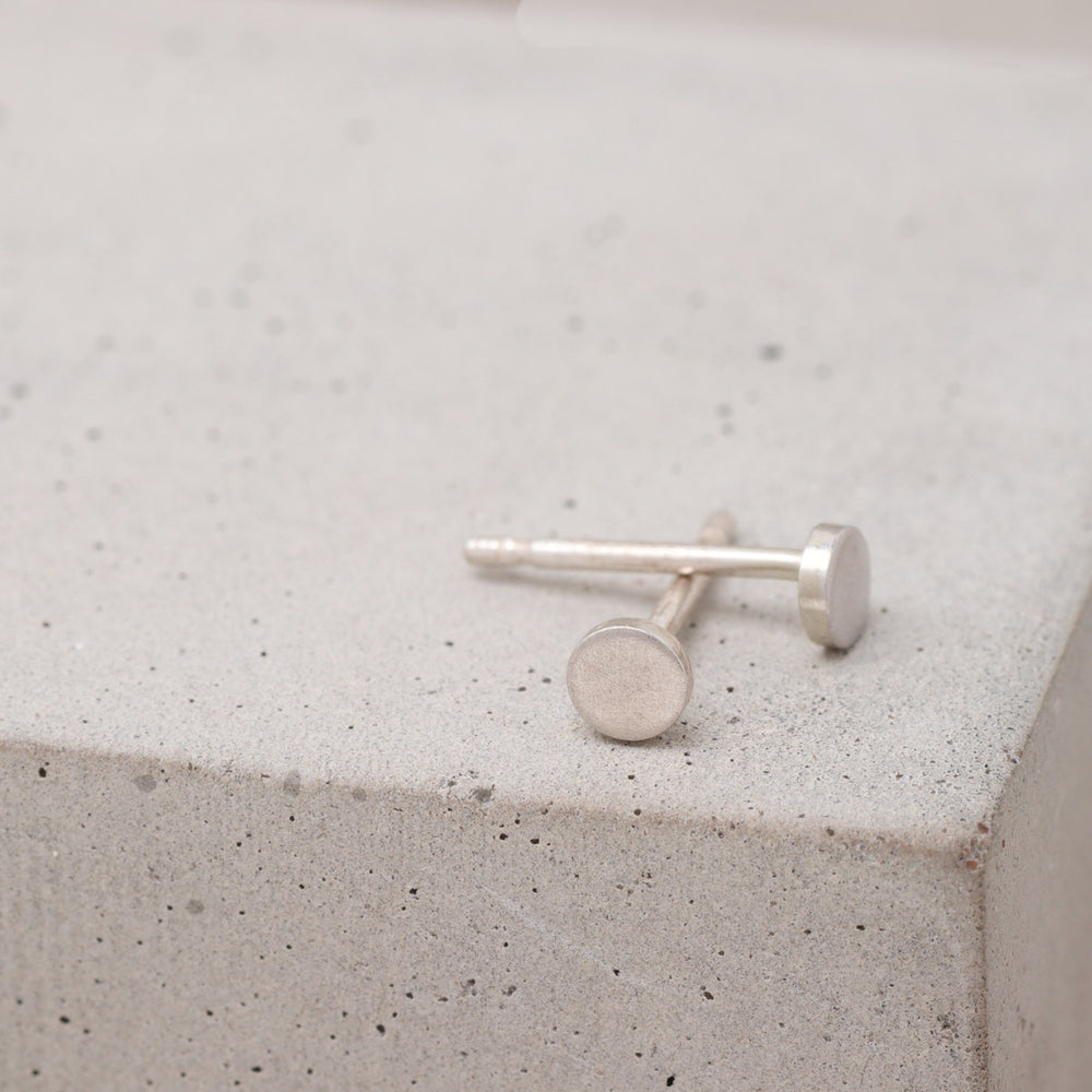 Tiny sterling silver circle stud earrings shown from the side