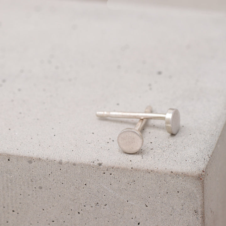 Tiny sterling silver circle stud earrings shown from the side